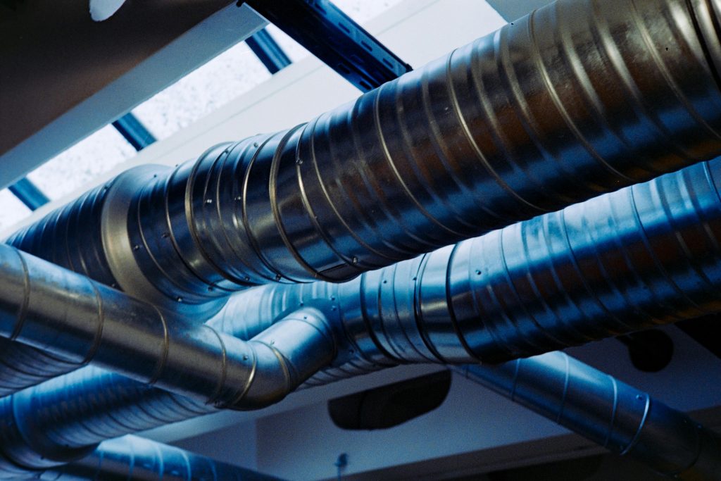 Exposed metal HVAC ductwork running along a ceiling, showing interconnected ventilation pipes used for air distribution in a building.